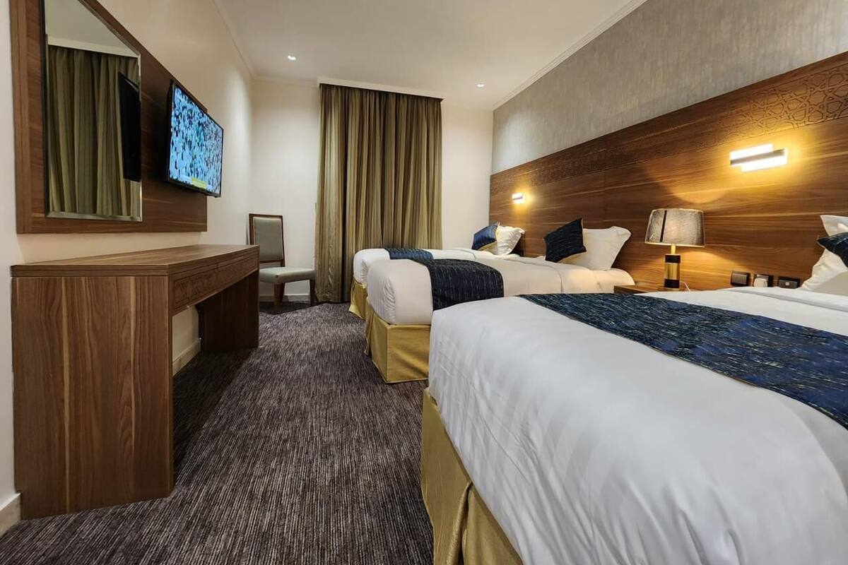 Ein Hotelzimmer mit zwei Betten, einem Schreibtisch, einem Fernseher und einem großen Spiegel.