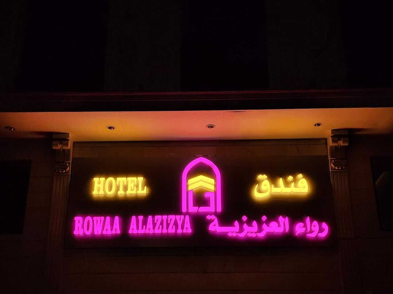 A hotel sign with the name "ROWAA ALAZIYA" in both English and Arabic, featuring a neon outline of a building.