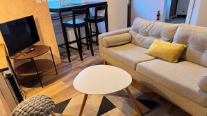 Un salon comprenant un canapé, une petite table ronde, un téléviseur et un coin repas avec des chaises.