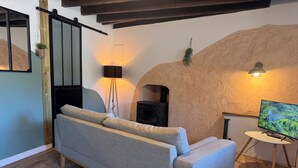 Un salon avec un canapé gris, une cheminée noire, un téléviseur posé sur un meuble blanc et un plancher en bois.