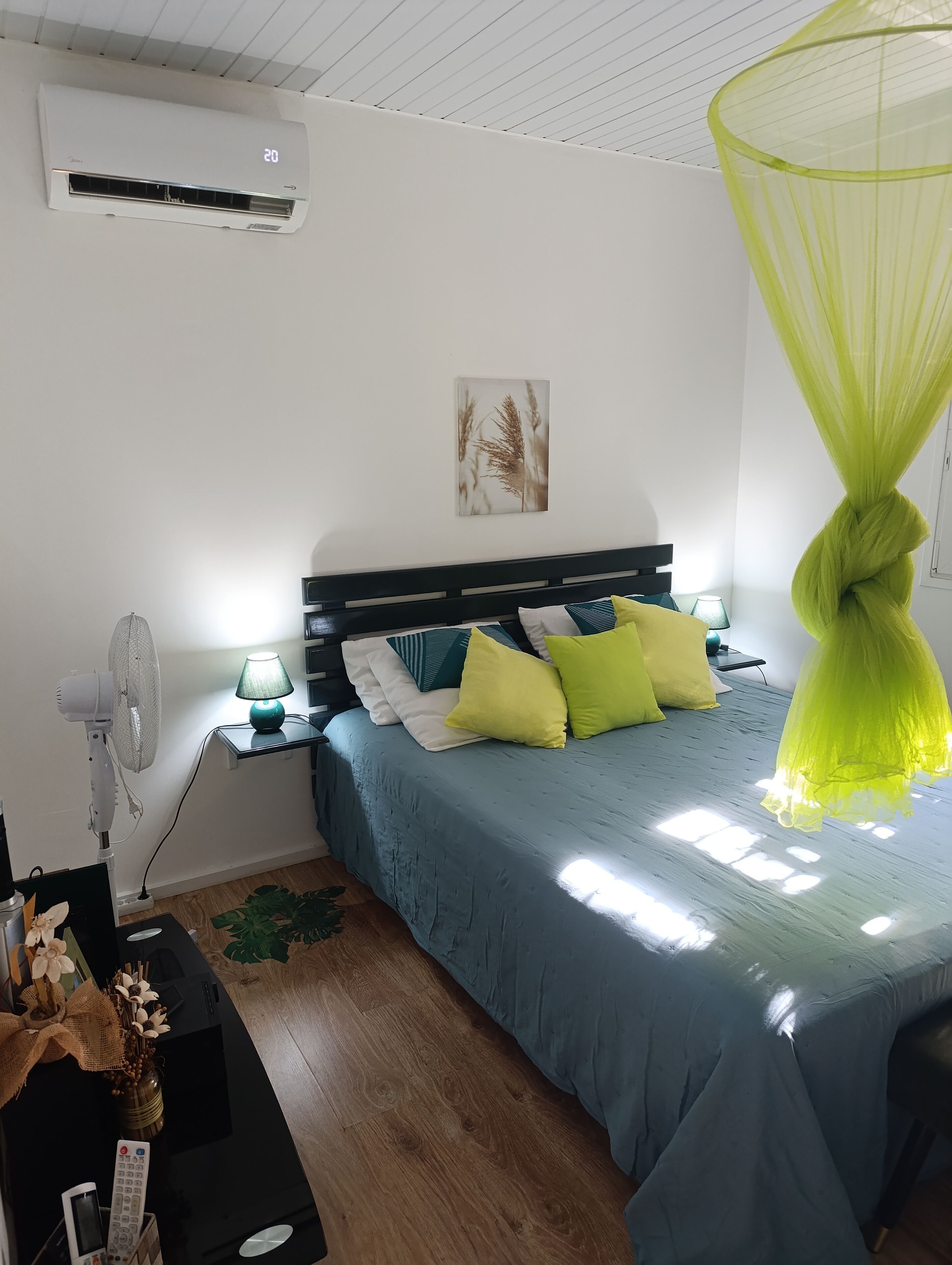 Een slaapkamer met een bed, nachtkastje, lamp, airconditioning en een decoratieve plant.