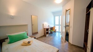 A hotel room with a bed, a desk, a chair, a mirror, and a view of the outside. - Comfort Single Room with Countryside View and Wi-Fi (Schlitz)