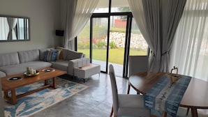 Un salon moderne comprenant un canapé, une table basse et une table à manger, de grandes portes-fenêtres coulissantes donnant sur un jardin et une vue sur l’extérieur.