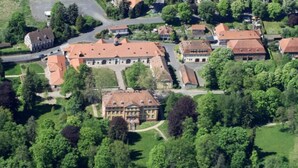 An aerial view of a residential area with multiple houses, a central building with a red roof, and surrounding greenery. - Comfort Double Room with Free Parking (Schlitz)