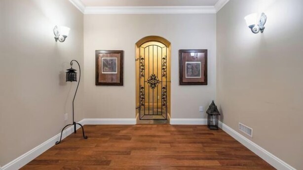 A hallway with wooden flooring, a decorative door, wall-mounted light fixtures, and framed pictures. - Vancouver Red House (Coquitlam)