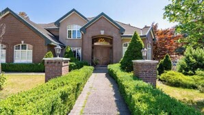 A two-story house with a brick facade, a central entrance with a door, and a pathway leading to the front door. - Vancouver Red House (Coquitlam)