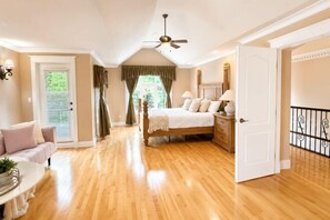 A bedroom with a wooden floor, a bed, a ceiling fan, a door, and a view of the outdoors. - Vancouver Red House (Coquitlam)