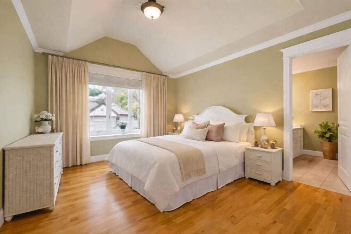 A bedroom with a bed, bedside tables, a window with curtains, a dresser, and a potted plant.