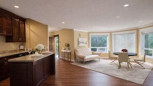 A spacious kitchen with dark wood cabinets, a marble countertop, and a large island. There is a dining area with a round table and chairs, and a beige sofa. - Vancouver Red House (Coquitlam)