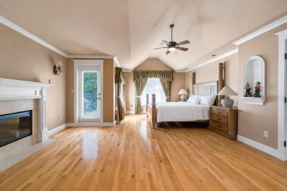 A bedroom with a fireplace, a bed, a nightstand, a mirror, and a ceiling fan.