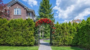 A pathway leading to a house with a brick facade and a red flower archway. - Vancouver Red House (Coquitlam)