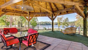 Un patio exterior con una pérgola de madera, sillas rojas, una mesa de vidrio y vistas a un lago.