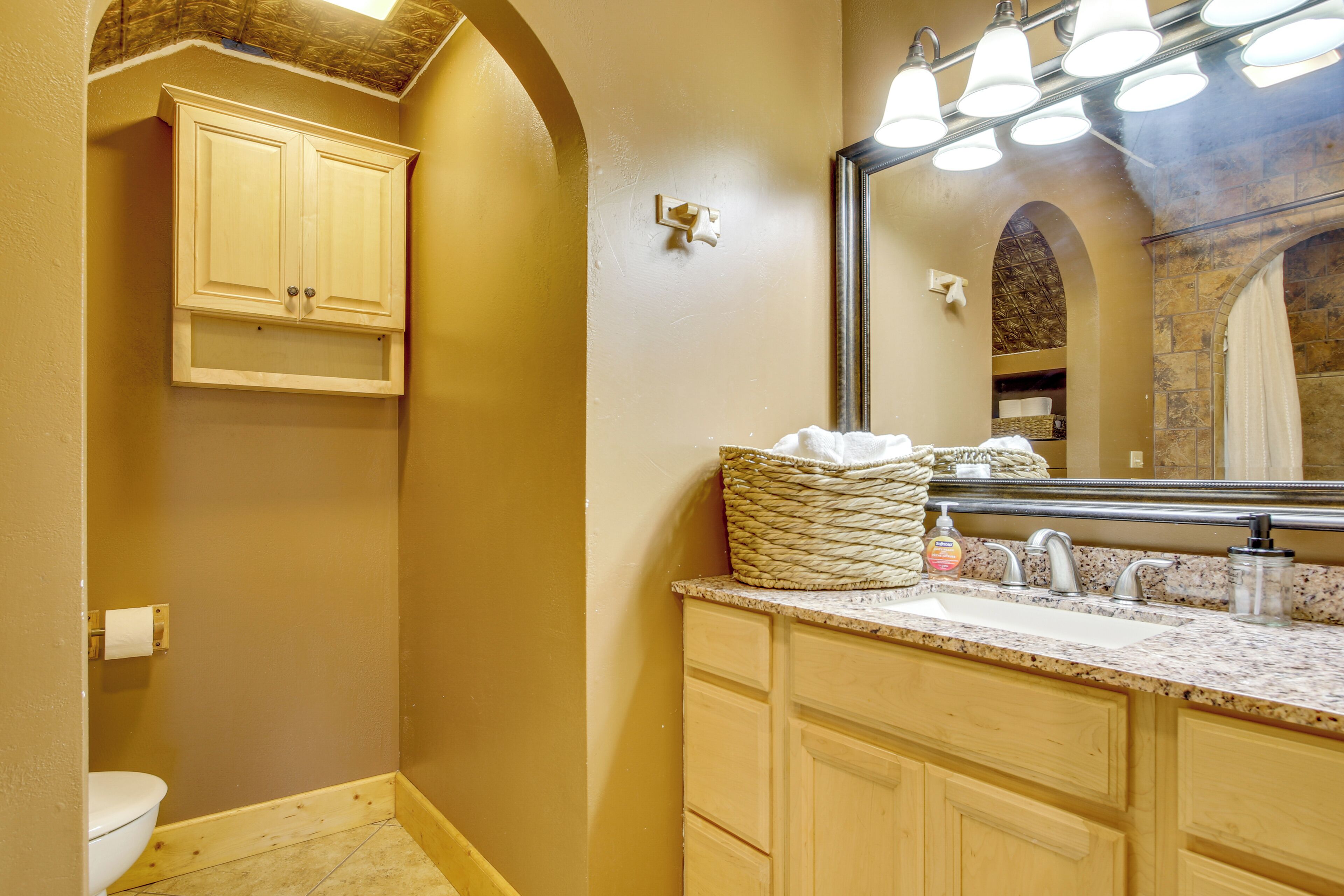 Un baño con pared beige, un inodoro blanco, un lavabo con encimera de mármol y un espejo con luces arriba.