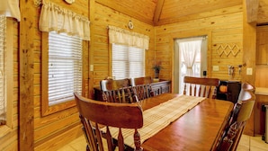 Interior de una cabaña de madera con una mesa de comedor, sillas y una zona de cocina.