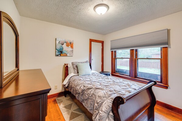 A bedroom with a wooden bed, a nightstand, a dresser, a painting, and a window with blinds. - 1 Mi to Akron Zoo: Ranch-Style Home w/ Yard! (Akron)