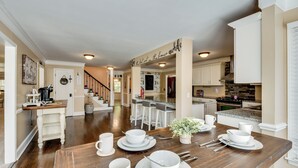 Een ruime keuken met een houten eettafel voor vier personen, witte kastjes en een centraal kookeiland met barstoelen.
