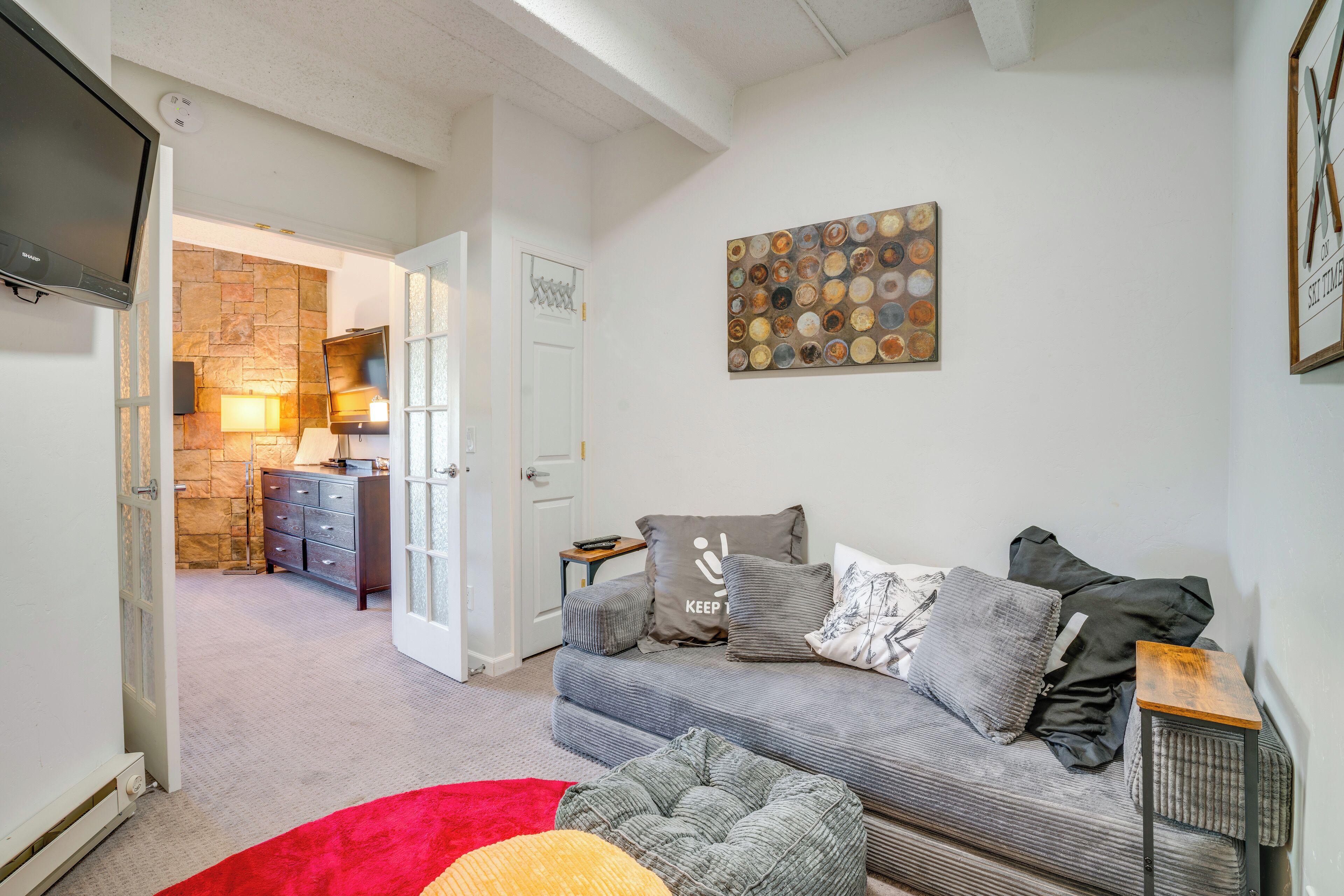 Een woonkamer met een grijze bank, een rood vloerkleed en een kunstwerk aan de muur.