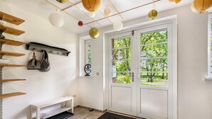 Un hall d’entrée propre et moderne, avec un banc, un paillasson et une porte donnant sur un jardin.
