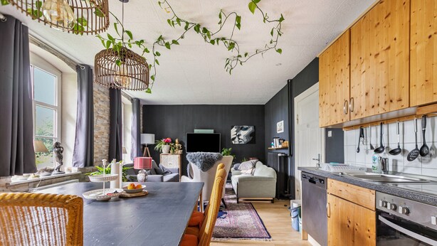Une cuisine moderne avec des meubles en bois, un coin repas doté d’une table noire et un espace de vie comprenant un canapé et un téléviseur.
