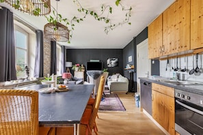Et moderne køkken med træskabe, et spiseområde med et sort bord og en opholdsstue med sofa og fjernsyn.