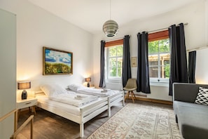 Et soveværelse med seng, stol, sofa, et vindue med gardiner, en radiator og et billede på væggen.
