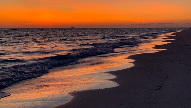 Una playa al atardecer con olas rompiendo suavemente en la orilla.