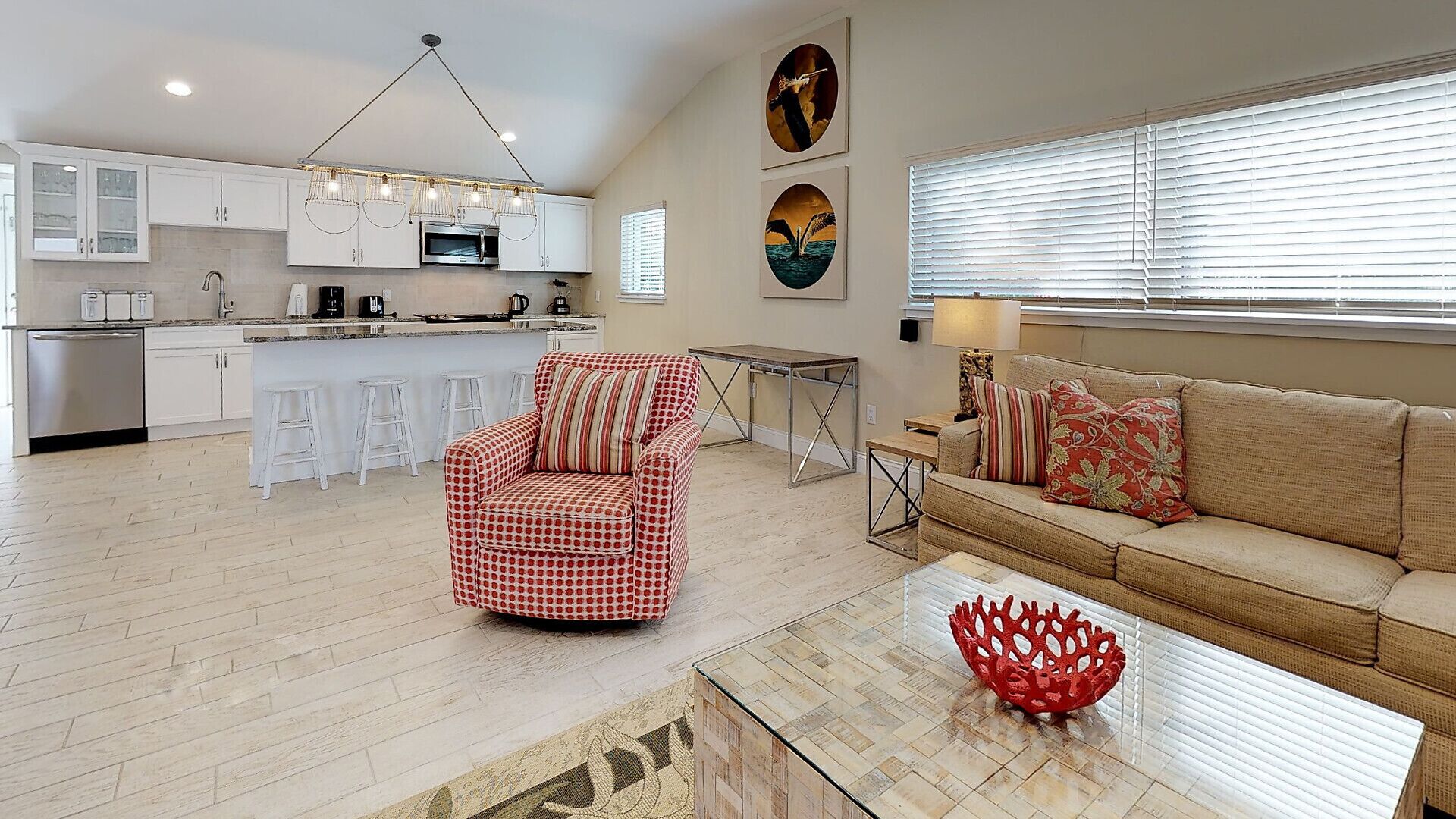 A modern living room with a sofa, a red patterned armchair, a coffee table, and a kitchen area with white cabinets and a microwave.