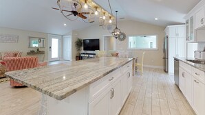 Una cocina amplia con una isla grande, armarios blancos y un ventilador de techo.