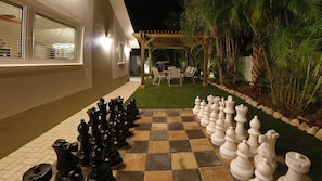Un jeu d’échecs installé sur une terrasse agrémentée d’une pergola et de mobilier d’extérieur.