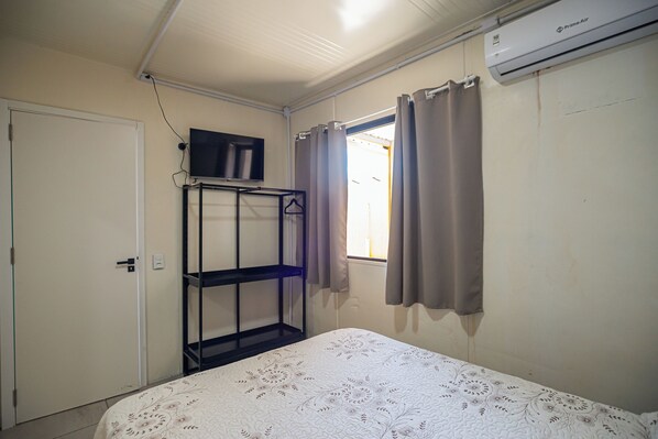 A bedroom with a bed, a TV on a shelf, a wardrobe, and an air conditioner. - Container 4 (Navegantes)