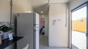 Ein schmaler Flur mit einem Kühlschrank, einem Sessel und einem Tisch mit einer Pflanze.