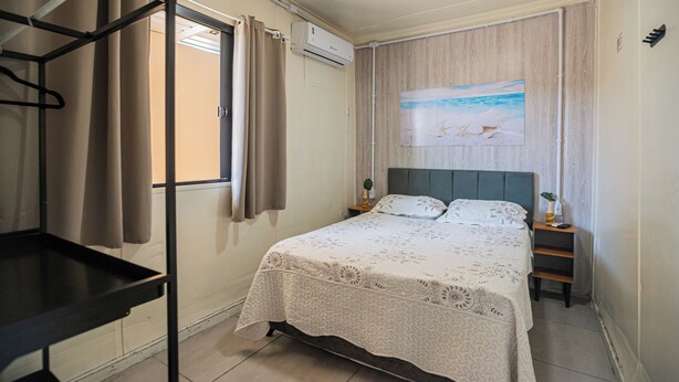 Ein ordentlich eingerichtetes Schlafzimmer mit einem Bett, einem Nachttisch, einer Wand-Klimaanlage und einem Fenster mit Vorhängen.