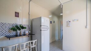 Eine Küche mit einem weißen Kühlschrank, einem kleinen Tisch mit zwei Stühlen und einer Zimmerpflanze auf einem Regal.