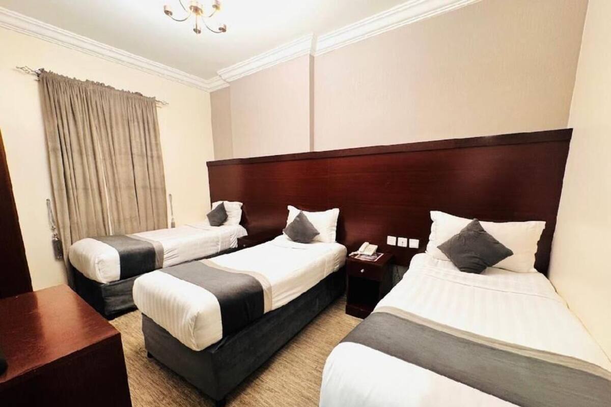 A hotel room with three beds, a wooden headboard, a bedside table, and a curtain.