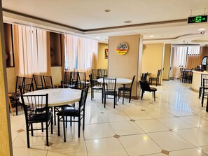 A restaurant with multiple tables and chairs, a clean tiled floor, and a wall with a circular sign. - Rowaa Makarem (Makkah)