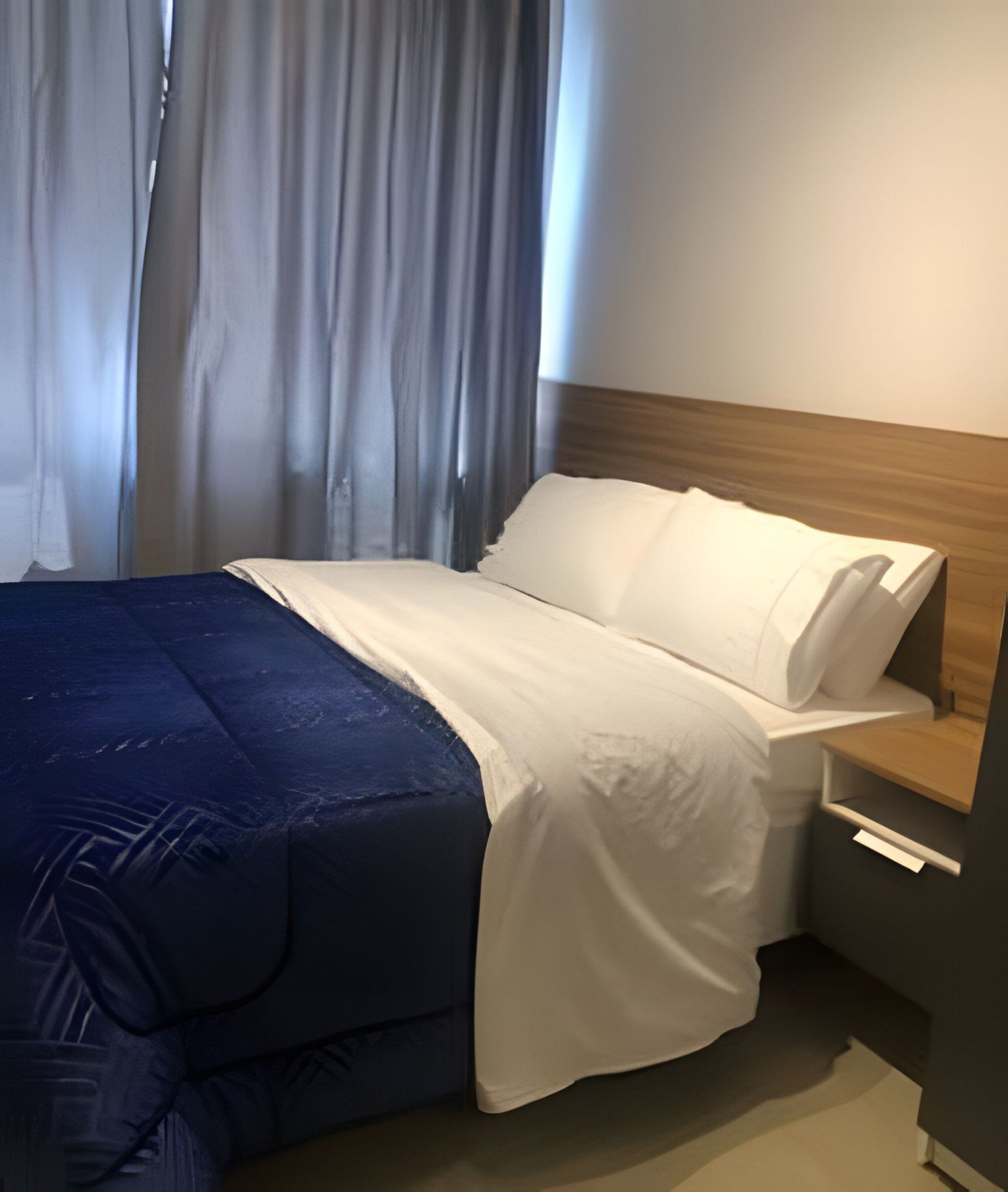 A hotel room with a bed, a nightstand, a wooden headboard, and a window with curtains.