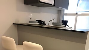 A kitchen with a grey island, two white bar stools, and a microwave above the counter. - Belgravia  (Porto Alegre)