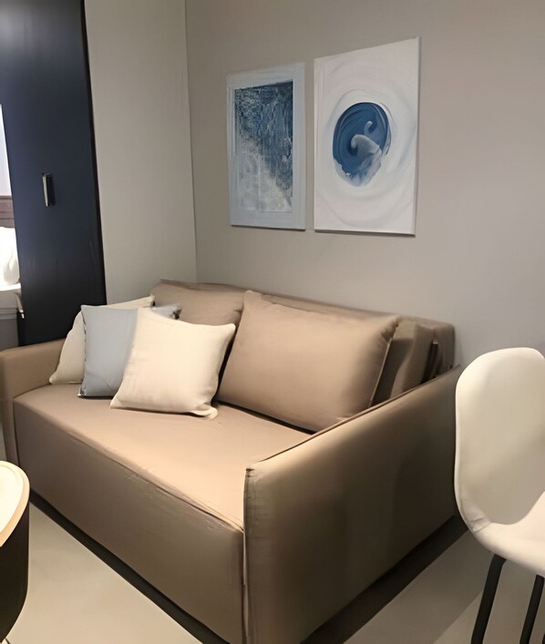 Un salon moderne avec un canapé beige, deux coussins et une chaise blanche. Deux tableaux abstraits sont accrochés au mur.