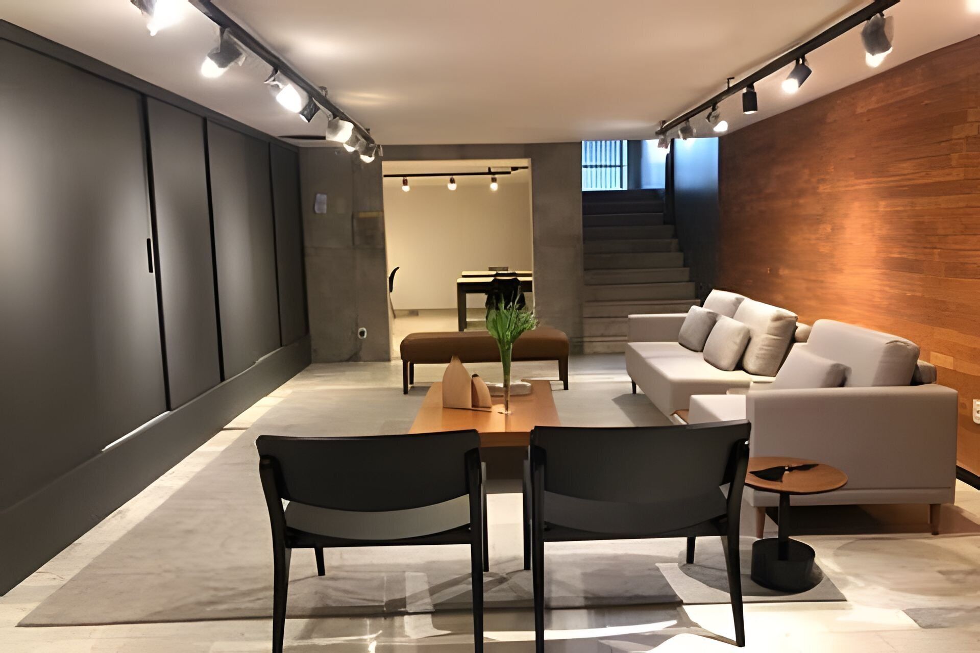 A modern living room with a sofa, two armchairs, a coffee table, and a dining table. There is a staircase leading to another level.