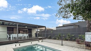 Ein Schwimmbad mit Terrassenbereich, überdachter Sitzgelegenheit und einem umzäunten Garten.