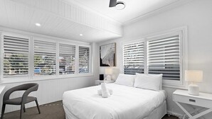 Ein Schlafzimmer mit einem großen Bett, einem Schreibtisch und zwei Fenstern mit Jalousien.