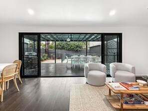 A modern living room with a large sliding glass door leading to an outdoor patio area. - Spacious 3-bedroom Home With Private Pool & BBQ (Newcastle)