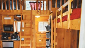 A compact cabin with wooden walls, a kitchenette, a bathroom, and bunk beds. - Pittsburgh Roaring Run RV Resort (Champion)