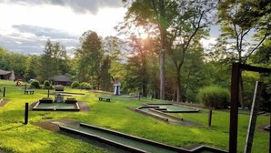 A miniature golf course with multiple holes, surrounded by trees and a few buildings in the background. - Pittsburgh Roaring Run RV Resort (Champion)