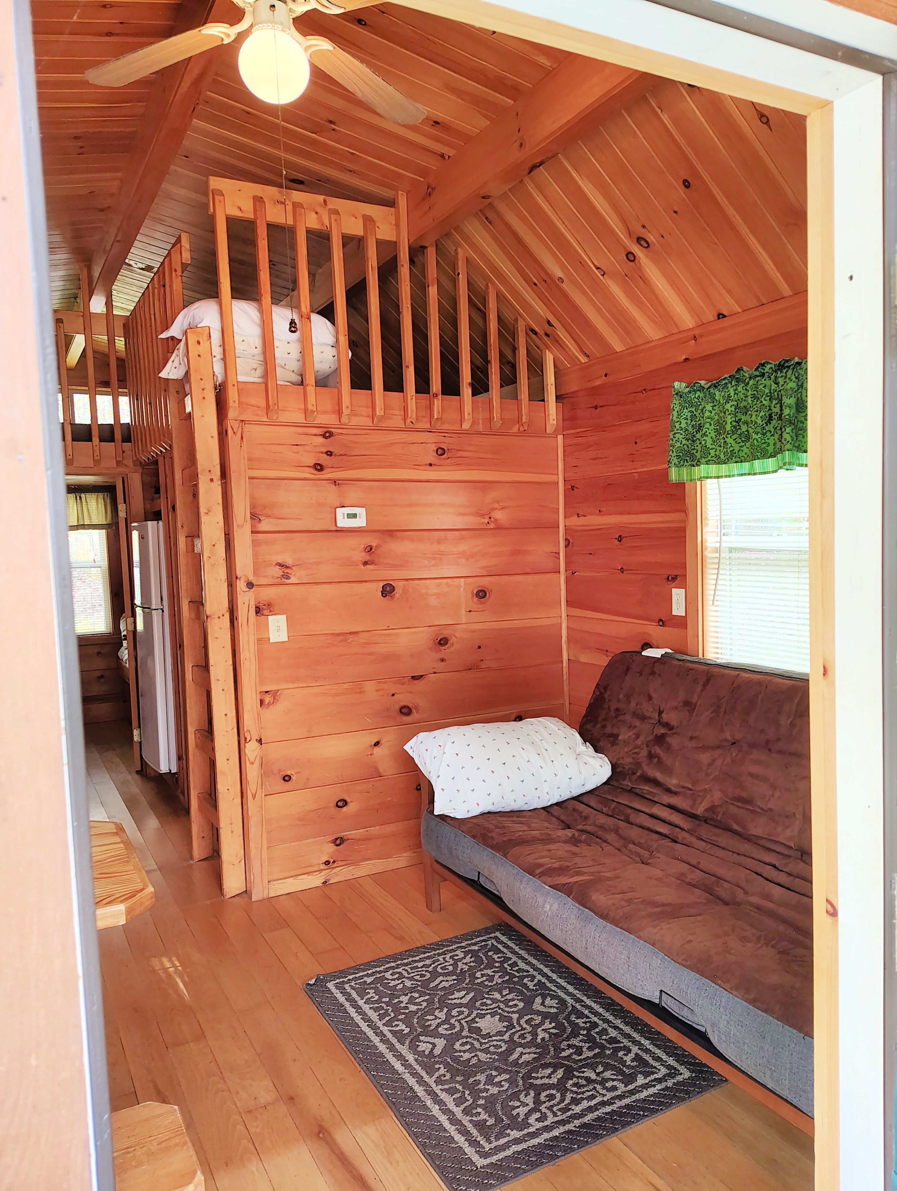 Interior acogedor de una cabaña con una litera, un sofá y un ventilador de techo.