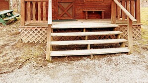 A wooden cabin with a porch, a sign indicating no smoking, and a bench. - Pittsburgh Roaring Run RV Resort (Champion)