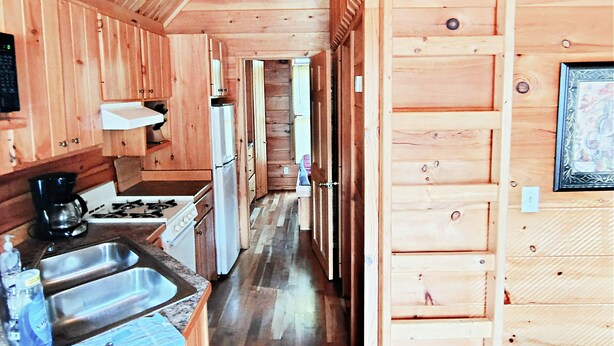 A wooden cabin interior with a kitchen, a dining area, and a loft space. - Pittsburgh Roaring Run RV Resort (Champion)