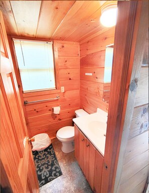 A small, wooden cabin bathroom with a toilet, sink, and window.
