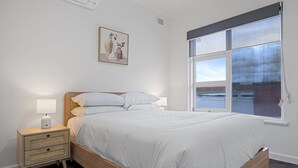 A bedroom with a wooden bed, white bedding, a bedside table with a lamp, and a window with a view. - 3-bed Campbelltown Stay With Private Balcony (Adelaide)