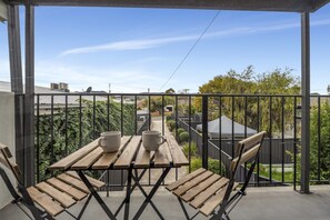 A balcony with wooden tables and chairs, a view of the neighborhood, and a clear blue sky. - 3-bed Campbelltown Stay With Private Balcony (Adelaide)